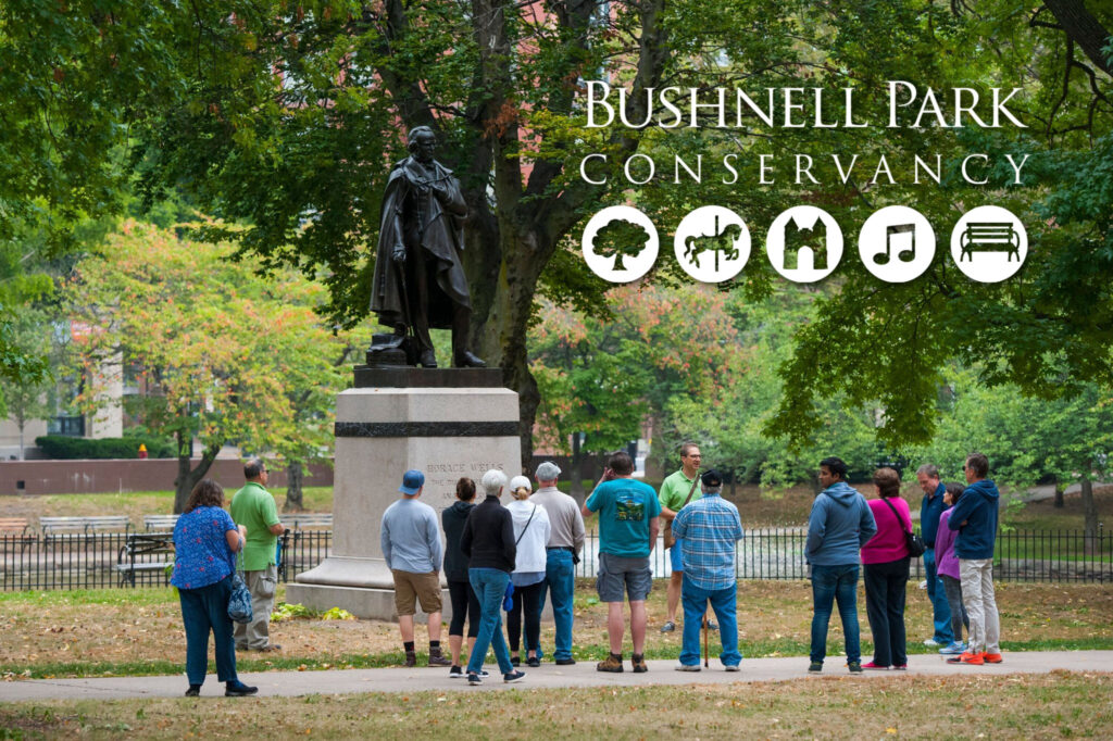 Photo of a group of Park visitors being led on a tour of Park monuments, in front of the statue of Horace Wells.